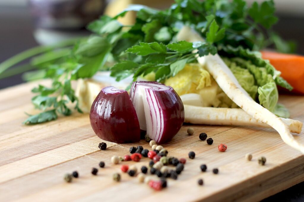 A red onion on a cutting board with multi-colored peppercorns