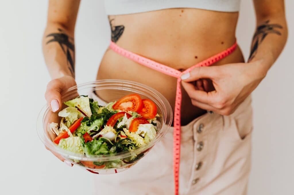 A woman holding a bowl of healthy salad shows off her shrinking waistline